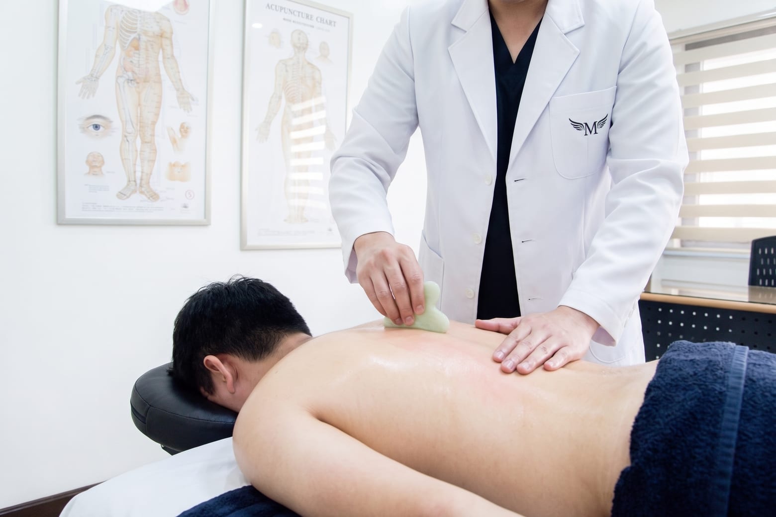 A practitioner drawing a jade gua sha tool down the muscle beside a patient’s spine.