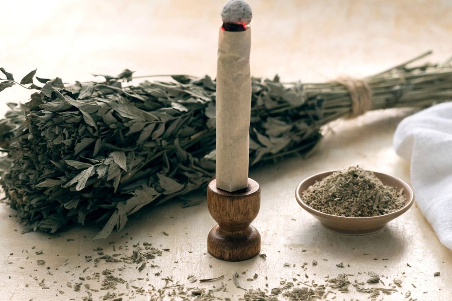 A lit moxa stick beside a bundle of dried mugwort and a bowl of loose herb.